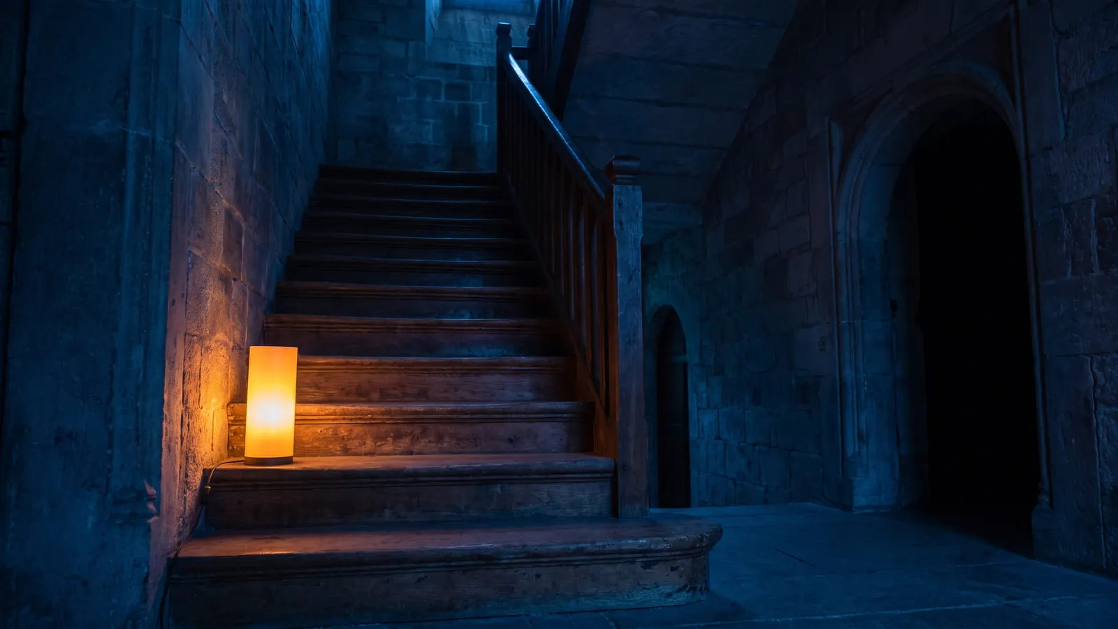 Erste Stufe einer Holztreppe im warmen Licht, die weiteren Stufen liegen im Dunkeln
