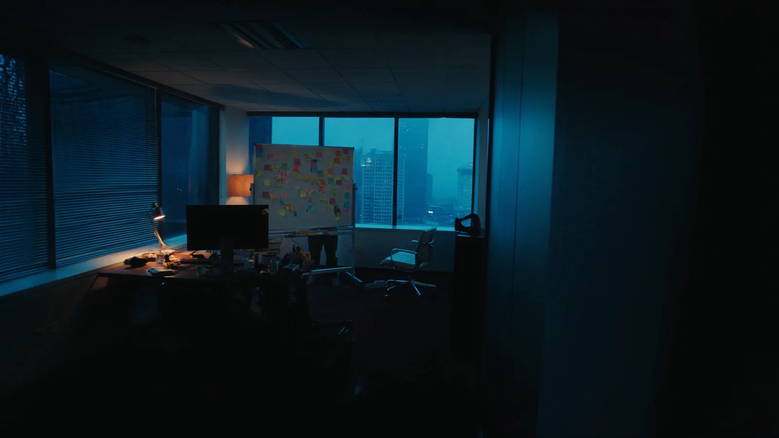 Whiteboard voller bunter Haftnotizen neben einem Schreibtisch im abendlichen Büro, eine warme Lampe