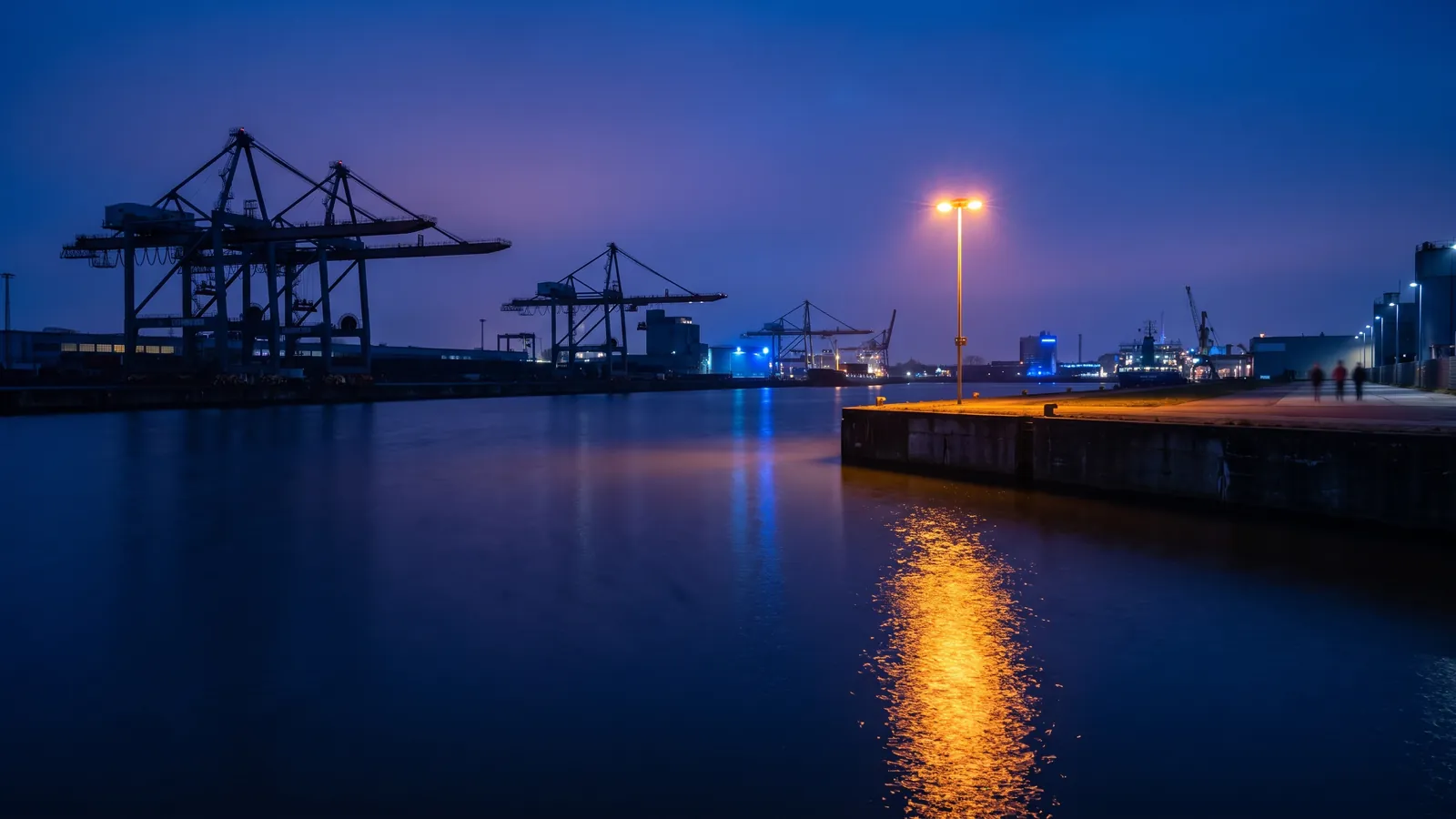 Hafenkräne am Rheinhafen in der Dämmerung, warmes Kailicht auf dunklem Wasser